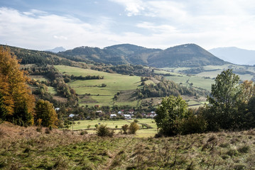 Fototapeta na wymiar autumn landscape of Kysuce region in Slovakia with Horny Vadicov village, meadows, fields, hills and blue sky with clouds
