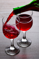 glass of red wine. Wine is poured into a glass from bottle on a light wooden background