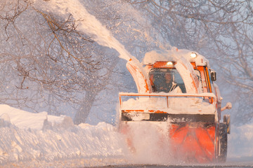 Snow truck cleaning snow from the road and streets working at sunset light on snowy day