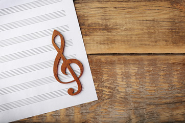 Treble clef and sheet of paper on wooden background