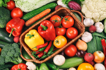 Wicker basket with fresh vegetables on background