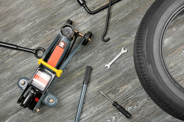 Car jack with tools and tire on wooden background