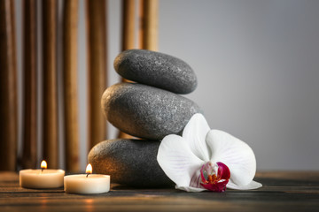 Spa still life with pebbles, candles and orchid flower on grey background