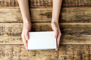 Female hands with white box on wooden background