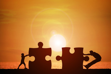 Silhouette of a man and children were pushed into jigsaw splice with beautiful sunset background, concept for business success and teamwork.