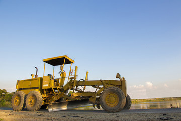 A huge yellow road grader parked on a roadside with clear blue sky as background