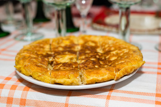 A just cooked Spanish omelette served in a dish over the table with some glasses in the background
