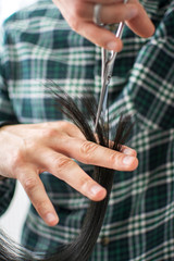 Male hairdresser cutting split ends on his female client at the hairdressing salon. Selective focus.