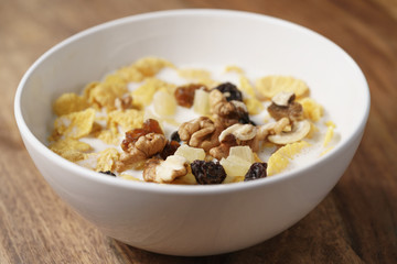 closeup photo of corn flakes with fruits and nuts in white bowl on wood table, simple healthy breakfast