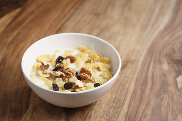 corn flakes with fruits and nuts in white bowl on wood table with copy space, healthy food