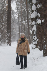 Portrait of senior woman fur coat and hat standing in cold winter snow covered forest, wide angle