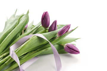 making bouquet from fresh purple tulips with ribbon on white background
