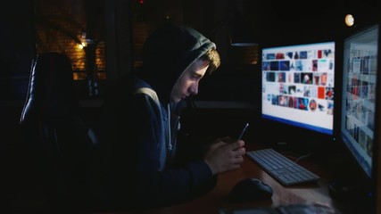 The guy of sixteen sitting near the computer late at night, using a mobile phone. Internet addiction in adolescents