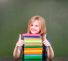 Happy schoolgirl in classroom showing thumbs up