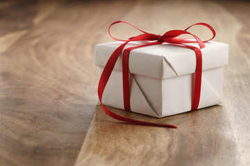 white paper gift box with thin red ribbon bow on old wood table, with copy space