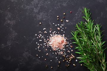 Rosemary plant, pink salt and spices on black stone table top view with copy space for menu or recipe, flat lay. © juliasudnitskaya