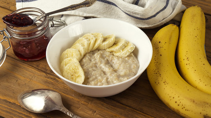 Bowl of oatmeal porridge with banana and jam on wooden background, healthy breakfast , diet food