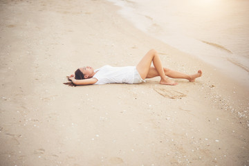 Young woman with white t-shirt lying down on the beach. Smiling