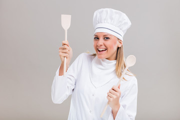 Happy female chef holding her work tool on gray background.
