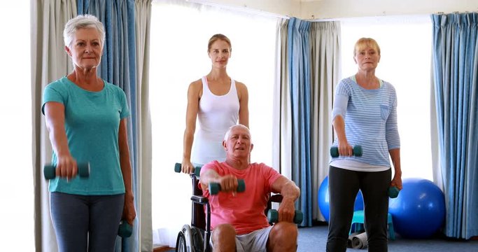 Trainer assisting senior citizens in performing exercise