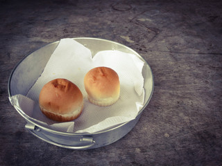 Two buns on white paper in a metallic tray placed on dark wooden background