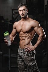 Fototapeta premium Handsome athletic fitness man holding a shaker and posing gym