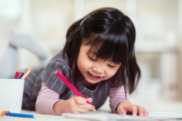 Pretty happy little japanese girl drawing with pencils at home