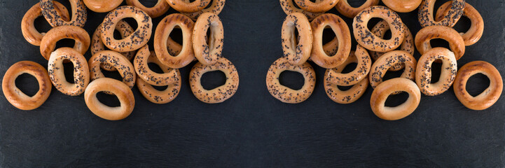 Bread poppy seed bagels on a black slate, Russian sushki, simple dessert for tea ceremony and beer party. Wide panoramic image.