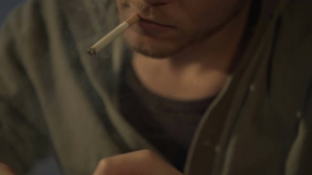 Young man lighting cigarette, drug and gaming addict playing on smartphone