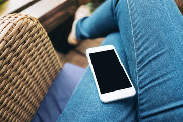 Mockup image of white mobile phone with blank black screen on woman's thigh