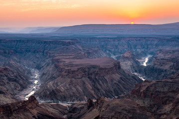 Fototapeta na wymiar Fish River Canyon, scenic travel destination in Southern Namibia. Last sunlight on the mountain ridges. Wide angle view from above.