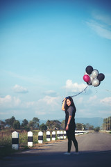 An asian woman holding balloons while walking along the road with blue sky background