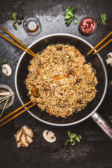 Spicy fried noodles in wok pan with chopsticks on dark rustic background, top view. Asian cuisine