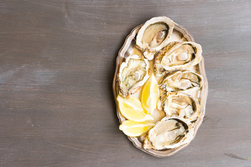 Plate of raw fresh open oysters shells with lemons, top view on wooden table with copy space