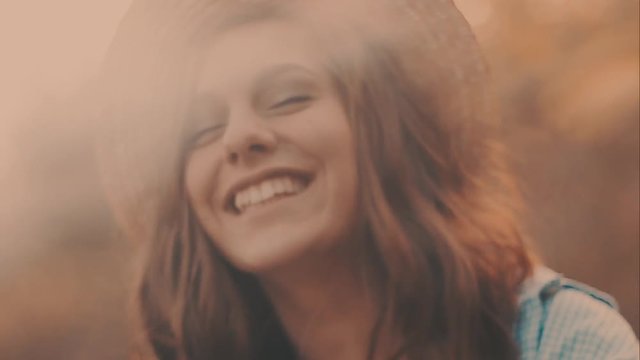 Close-up portrait of a beautiful young girl with long dark hair wearing straw hat. She plays with her hair in the warm rays of setting sun.