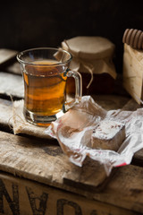 Glass cup with hot tea with jar of honey or jam, wood spoon, Spanish cookie polvoron on  vintage box, black wall background,rustic countryside interior,cozy atmosphere