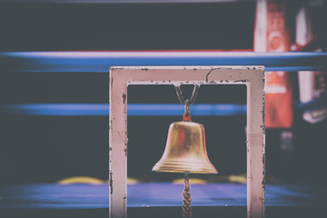 Brass Boxing Bell Suspended on Metal Frame With Blurry Fighting Ring in Background