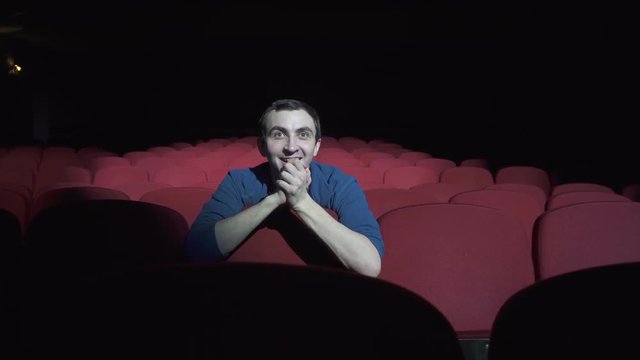 Man sitting in comfortable red chairs in dark cinema theater and applauds