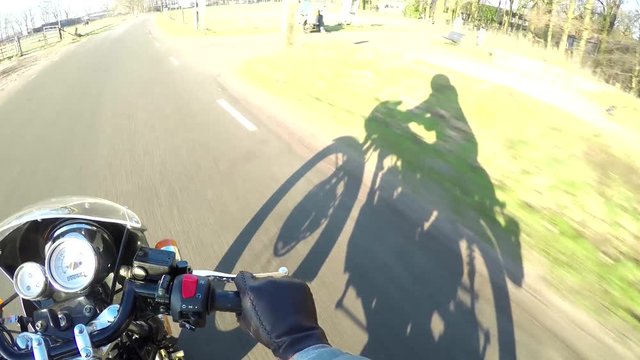 Motorcycle ride first person view helmet camera FPV shadow right fast on classic vintage cafe racer motorbike handlebar with dials above sunny day riding on rural road driver wearing leather gloves 4k