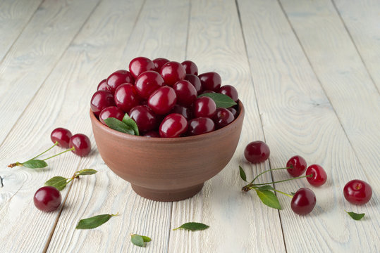 ripe cherries and leaves in a bowl on a textured wooden background