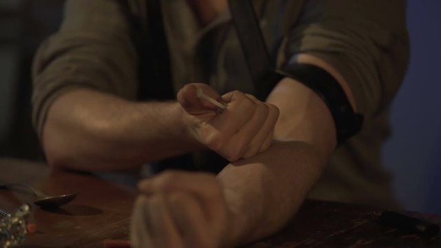 Addicted man injecting heroin dose in vein with syringe for drug withdrawal
