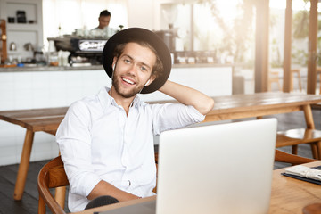 Happy young hipster wearing white shirt and stylish hat having cheerful face expression, smiling...