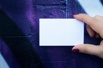 Female hand holding blank white business card over colorful background.