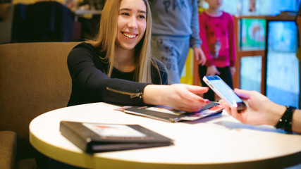 woman in cafe. young girl sitting at table smiling, transmits smartphone girlfriend in  black dress