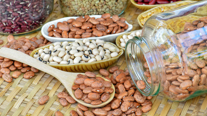 Pinto bean on wooden spoon with various legumes in container