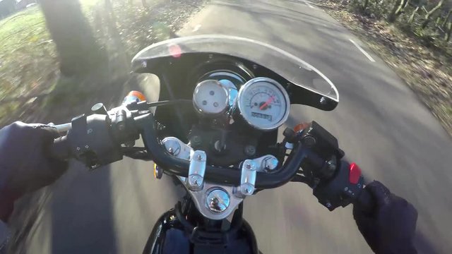 Motorcycle ride first person view helmet camera FPV riding very fast on classic vintage cafe racer motorbike handlebar with dials above sunny day riding on rural road driver wearing leather gloves 4k