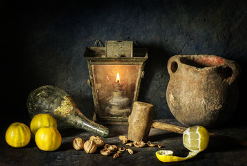 Classic still life with fresh lemon placed with old glass bottle,vintage pottery jag,illuminated lamp,nuts and wooden hammer on rustic dark background.. © dinasaeed