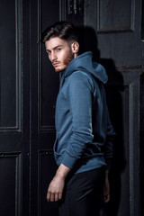 Handsome fashion model man posing wearing hoodies jacket near the wooden wall