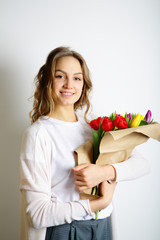 Smiling young woman standing with a bouquet of tulips in hands,