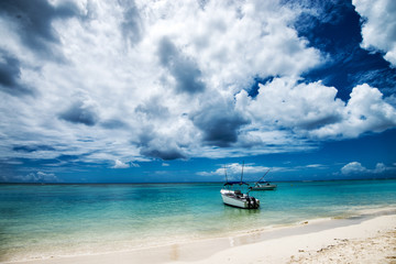Fototapeta na wymiar Paradise island, boats on crystal clear water under beautiful clouds.